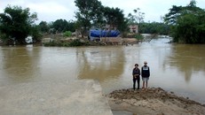 Hai mẹ con bà Nở đứng một góc nền ngôi nhà đã bị lũ dữ biến thành nhánh sông sâu. 