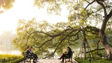 Vài người đi bộ ngồi nghỉ chân bên bờ Hồ Gươm tận hưởng ánh nắng ấm áp.