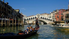Một người chèo thuyền lướt qua cầu Rialto, băng qua kênh Grand Canal .