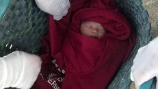 Bé trai sơ sinh được quấn trong chiếc áo ấm màu đỏ và để trong chiếc túi màu xanh, bỏ trước nhà một người dân.