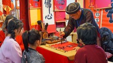 Các bạn nhỏ chăm chú xem ông đồ cho chữ tại Văn Miếu – Quốc Tử Giám. Ảnh: TTXVN