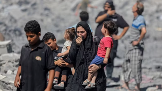 Người dân Palestine đứng trên đống đổ nát sau các cuộc không kích của Israel xuống Dải Gaza. 