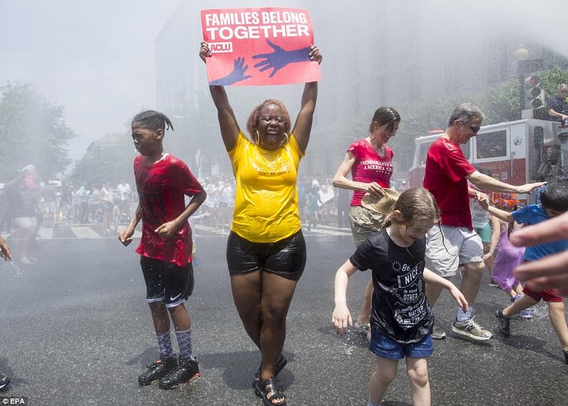 A woman holds a sign while joining others underneath water being sprayed by a firetruck to cool off people attending a 'Families Belong Together' rally, in Washington DC SaturdayÂ