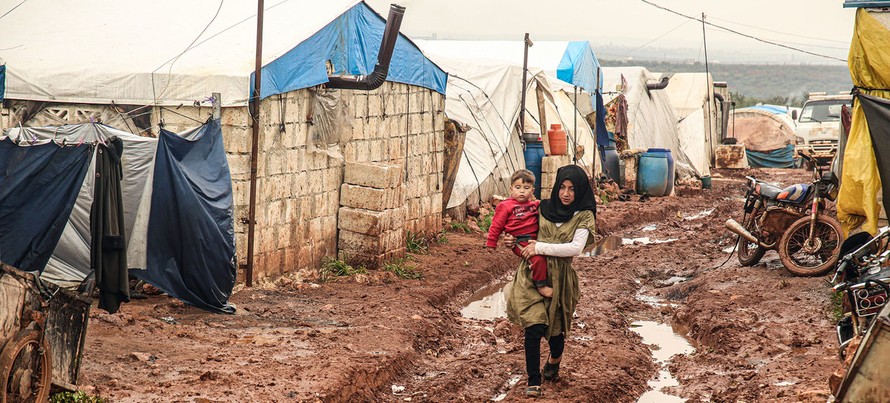 Một cô gái đi bế em trai đi qua vũng bùn lầy tại trại Khair Al-Sham IDP, Idlib Governorate, Syria. Ảnh: UNOCHA.