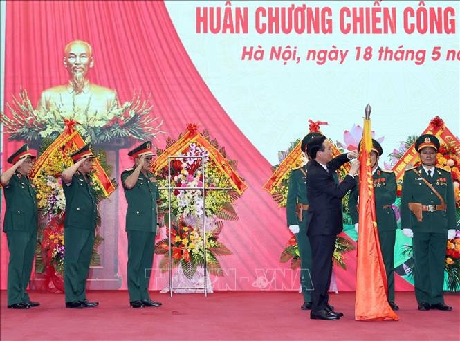 Chủ tịch nước Võ Văn Thưởng gắn Huân chương Chiến công hạng Nhất lên lá cờ truyền thống của Tổng Cục II, Bộ Quốc phòng. Ảnh: Thống Nhất/TTXVN