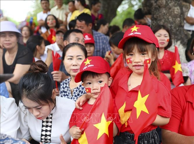Những em nhỏ với trang phục rực rỡ cờ hoa theo người lớn đi xem diễu binh, diễu hành.