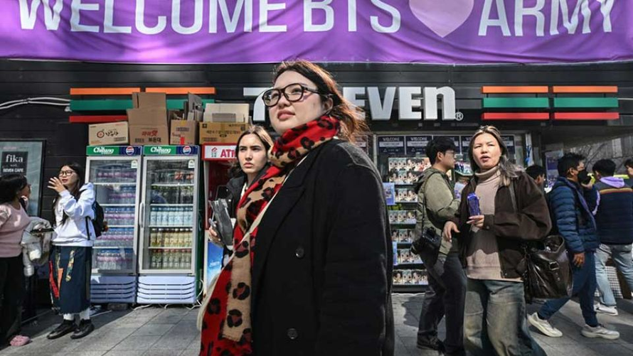 Người dân đi ngang qua một cửa hàng tiện lợi treo băng rôn chào đón người hâm mộ BTS, gần địa điểm diễn ra đêm nhạc tái xuất của BTS tại trung tâm Seoul hôm 21/3/2026. Ảnh: AFP.