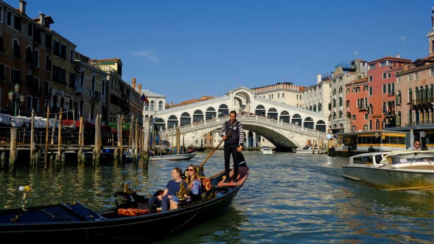 Một người chèo thuyền lướt qua cầu Rialto, băng qua kênh Grand Canal .