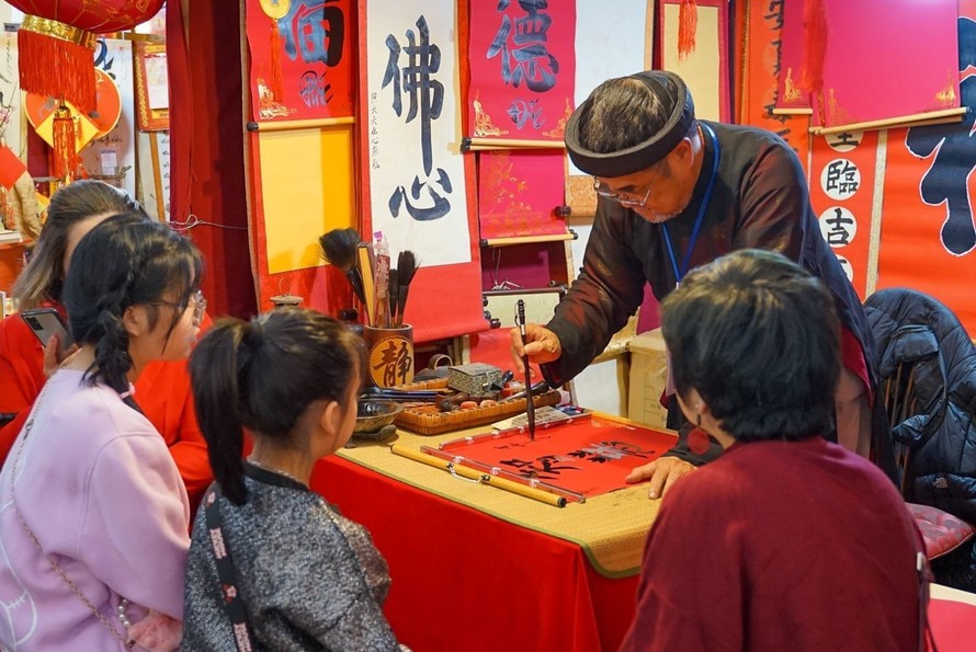 Các bạn nhỏ chăm chú xem ông đồ cho chữ tại Văn Miếu – Quốc Tử Giám. Ảnh: TTXVN