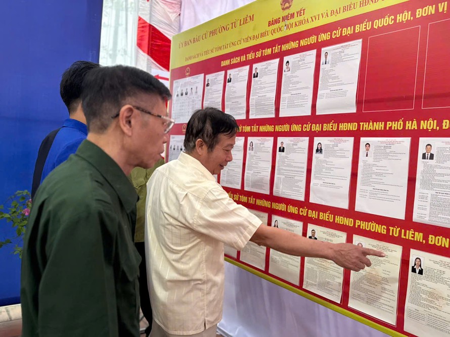 Cử tri và cán bộ trong tổ bầu cử tham khảo danh sách các đại biểu. 