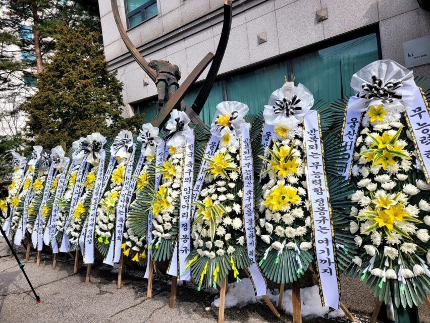 Trụ sở SM Entertaiment bao quanh bởi những chiếc hoa tang. Ảnh: Koreaboo.